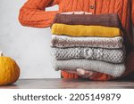 A woman holding a stack autumn warm knitted sweaters. Change of season and wardrobe. autumn slow fashion concept