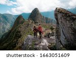 Small photo of Couple dressed in ponchos watching the ruins of Machu Picchu