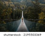 Young traveler man dressed in yellow jacket crosses hiking on an impressive wooden and metal bridge in the village of Goms in the Swiss alps