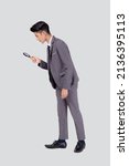 Small photo of Young asian business man in suit look at magnifying glass for search isolated on white background, businessman expression and find quality, full length, inspector and scrutiny, male expression.
