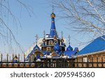 Small photo of Christian church behind the fence in winter through the branches of trees, golden domes and crosses of the temple, the theme of religiosity and faith in God, wooden church