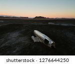 Aerial of a crashed old airplane on a black sand beach in southern Iceland during sunset.