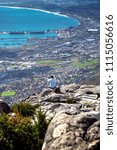 Small photo of A lonely man sits on top of a rock Table Mountain in thought and looks at the disreputable appearance of Cape Town.