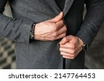 A man fastens a button on a gray coat jacket. Stylish men's accessories up close. Businessman holds hands together.