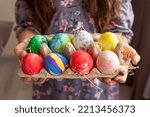 Hands of a girl in a dress holding a cardboard tray with colorful hand-painted eggs