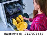 Housewife woman uses modern dishwasher for wash dishes and glasses at home kitchen