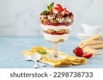 Strawberry tiramisu in a glass bowl on a blue background. Summer berry dessert trifle. Selective focus. Copy space
