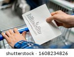 person's hands holding a shopping list paper sheet and check buying products in grocery store
