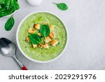 Green Cream Soup. Spinach broccoli creamy soup with croutons on gray stone background. Top view with copy space.