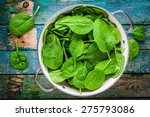 raw fresh spinach with drops in a colander on a rustic wooden table