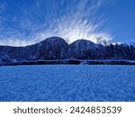 Winter sunrise in Austrian Alps. Winter sunshine over snowy mountains. Snowy panorama with the Austrian Alps, the green coniferous forests and a valley covered by white snow.