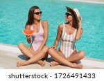 Fashion portrait of two stunning girls laying near pool, amazing long blonde and brunette hair, stylish bikinis, pretty faces tanned slim body,eating watermelon , vacation