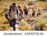 Small photo of Millennial African American man leading friends hiking single file uphill on a path in countryside
