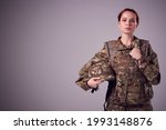 Studio Portrait Of Serious Young Female Soldier In Military Uniform Against Plain Background