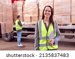 Small photo of Portrait Of Female Freight Haulage Manager Standing By Truck Being Loaded By Fork Lift