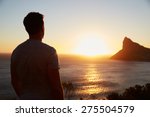 Silhouette Of Man Watching Sun Set Over Sea And Cliffs