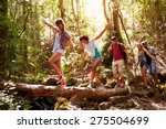 Group Of Friends On Walk Balancing On Tree Trunk In Forest