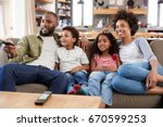 Family Sitting On Sofa In Open Plan Lounge Watching Television