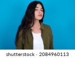 Small photo of caucasian girl wearing trendy clothes standing over blue background with snobbish expression curving lips and raising eyebrows, looking with doubtful and skeptical expression, suspect and doubt.