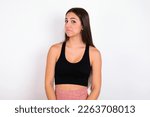 Small photo of young woman wearing sportswear over white studio background with snobbish expression curving lips and raising eyebrows, looking with doubtful and skeptical expression, suspect and doubt.