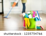 Small photo of Cleaning items on floor in modern kitchen. Woman maid or charwoman blured in background. Bucket, brush, washcloth, spray.