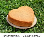 Freshly baked heart-shaped cake on a plate, placed outside in the garden to cool down