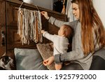 Small photo of mom and daughter baby up to 1 year in gray clothes. Interior in boho style, handmade decor. mom and daughter home atmosphere. Snuggery. Baby reaches for macrame