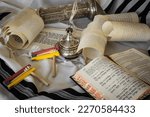 Small photo of Tiberias, Israel. 01.01.23: The Scroll of Esther and Purim Festival objects [Megillah, Hamantash, coins, flowers, siddur] on against the background of a prayer shawl (Tallit).