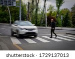 Pedestrian walking on zebra crossing and a driving car failing to stop in blurred motion. Pedestrian reacts with hand to the driver.
