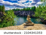 Stacked stones or obo against wonderful landscape of quarry with turquoise water in northern forest on summer day. Beautiful scene, nature of russian north. Ruskeala marble canyon, Karelia, Russia.