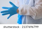 Small photo of Close-up of putting on surgical gloves. A medical worker in a disposable washing gown puts on blue latex gloves to work in an infected area or before a surgical intervention. Caronovirus.