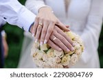 Wedding rings on the hands of the newlyweds, a bouquet of flowers in the background. Gold rings on the hand of a man and a woman