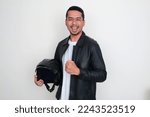 Asian man wearing black leather jacket holding motorcycle helmet with excited expression
