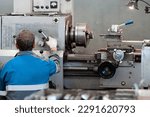 Turner at lathe in workplace. View of worker from back. Metal processing in lathe shop. Equipment adjuster..