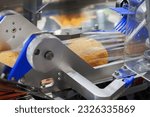 Small photo of baked bread in food grade plastic bag on conveyor belt moves to seal in packing machine at production line of bakery manufacturing factory. food processing and industry concept.