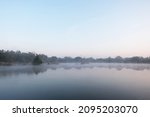 Dawn over the foggy lake. Beautiful dreamy view. Blue sky just before the sunrise and fog over water and trees with reflections on the river bank.