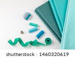 Small photo of Apportion of sewing tools and sateen fabrics in similar tones on a white background. It is complemented with accessories: a measuring green tape, a needle case, a thimble and coils with threads