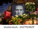 Small photo of Vilnius, Lithuania - February 20 2024: Flowers and candles laid at spontaneous memorial for Russian opposition leader Alexei Navalny, with black and white portrait wet from the snow and raindrops