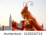 Beautiful costume of woman in red and orange colours at Venice carnival, gondollas, sea and basilica San Giorgio Maggiore at the background