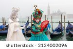 Beautiful costume of womans in green and white colours in Venice, there is a sea, gondollas and basilica San Giorgio Maggiore at the background, fog weather