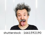 Small photo of Portrait of jocular aging man with grey long hair sticking his tongue out in Einstein manner