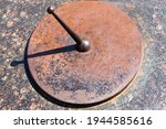 Small photo of A sundial dial with a gnomon and a shadow from it. Old rusty surface without numbers