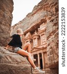 Small photo of Caucasian tourist traveler sitting on viewpoint in Petra ancient city looking at the Treasury or Al-khazneh, famous travel destination of Jordan. UNESCO World Heritage site
