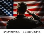 Memorial day. A uniformed soldier salutes against the background of the American flag. Rear view. Dark colors. The concept of the American national holidays and patriotism
