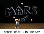 Mars colonization. Figure of astronaut with victoriously raised hands. In the background, a chalky black board with the inscription MARS.