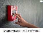 Activate fire alarm trigger system which is installed on granite wall of the building. Human action scene photo, selective focus.
