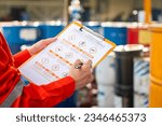 Small photo of Action of safety officer is using a pen to checking on the hazadous material symbol label form with the chemical barrel as blurred background. Safety industrial working scene concept. Selective focus.