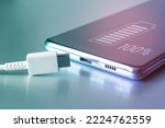 Fully charged battery icon on the touch screen of the cell phone and a USB Type-C cable. Fully charged smartphone battery. Keeping the battery intact. Battery safety. Copy space