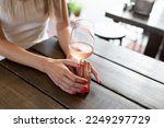 Woman's hands with red manicure holding a glass of wine. Glass of wine in women's hands against a wooden table. Focusing on the hands. Close-up.