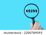 Small photo of Focused on learning English language. English word Nouns part of speech under magnifying glass. Grammar content for teacher and student.